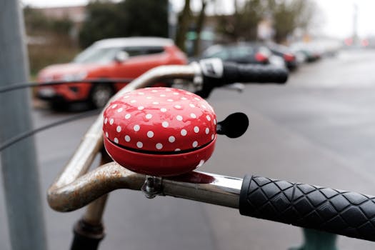 Close-up of a red polka dot bicycle bell on a handlebar, urban street scene.