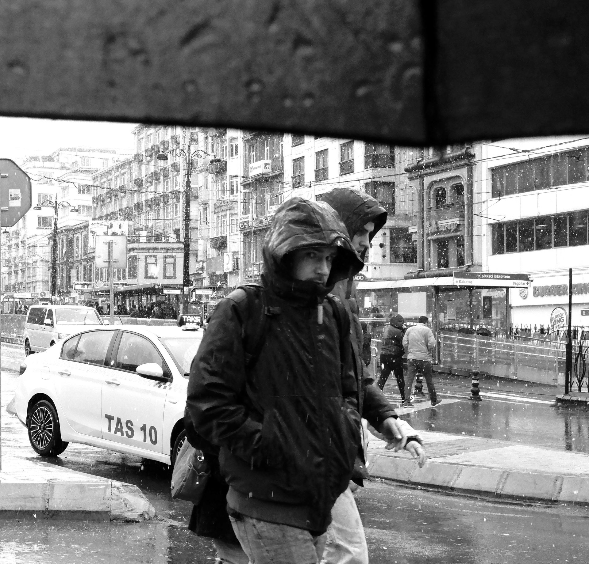 Black and white urban street scene with pedestrians and taxis during rainy day.