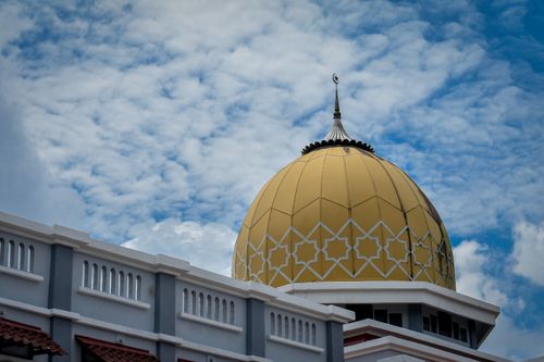 Free Architectural shot of a mosque's golden dome against a vibrant blue sky. Stock Photo