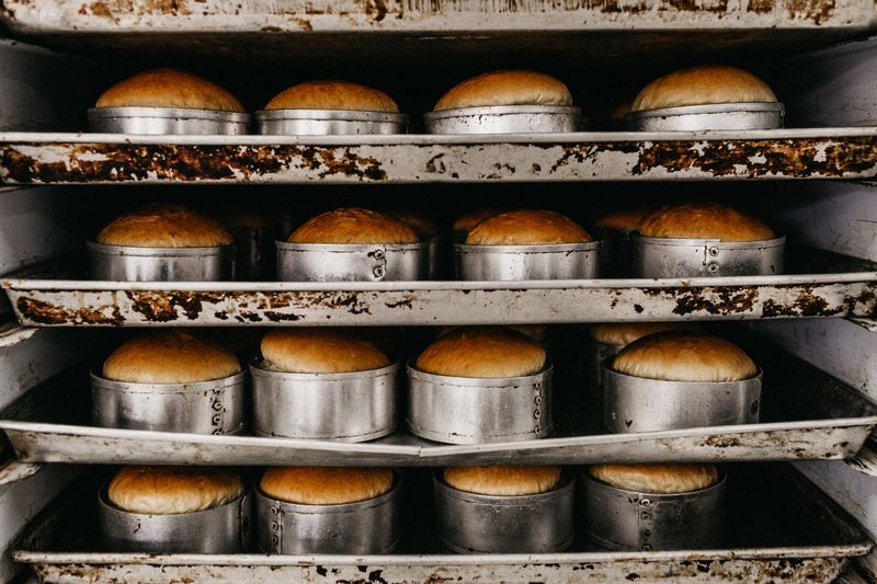 Rows of golden bread rolls in metal trays, showcasing industrial baking setup.