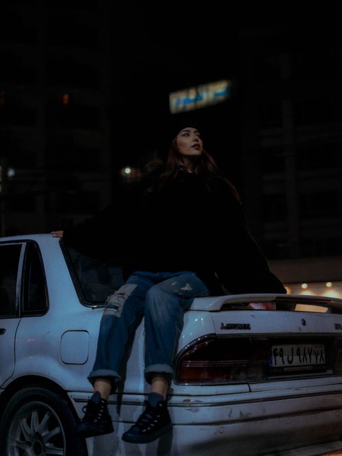 Free A stylish woman seated on a car at night in an urban setting, exuding a moody vibe. Stock Photo