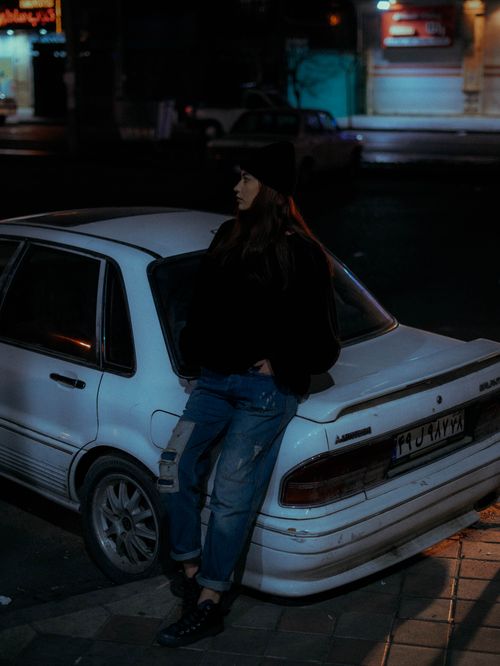 Free Moody night portrait of a woman leaning on a white car in the city. Stock Photo