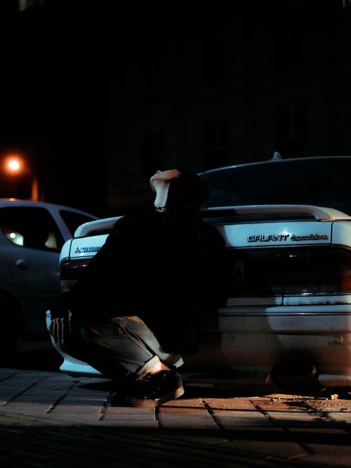 Free A person leans against a car in a dimly lit street at night, creating a moody ambiance. Stock Photo