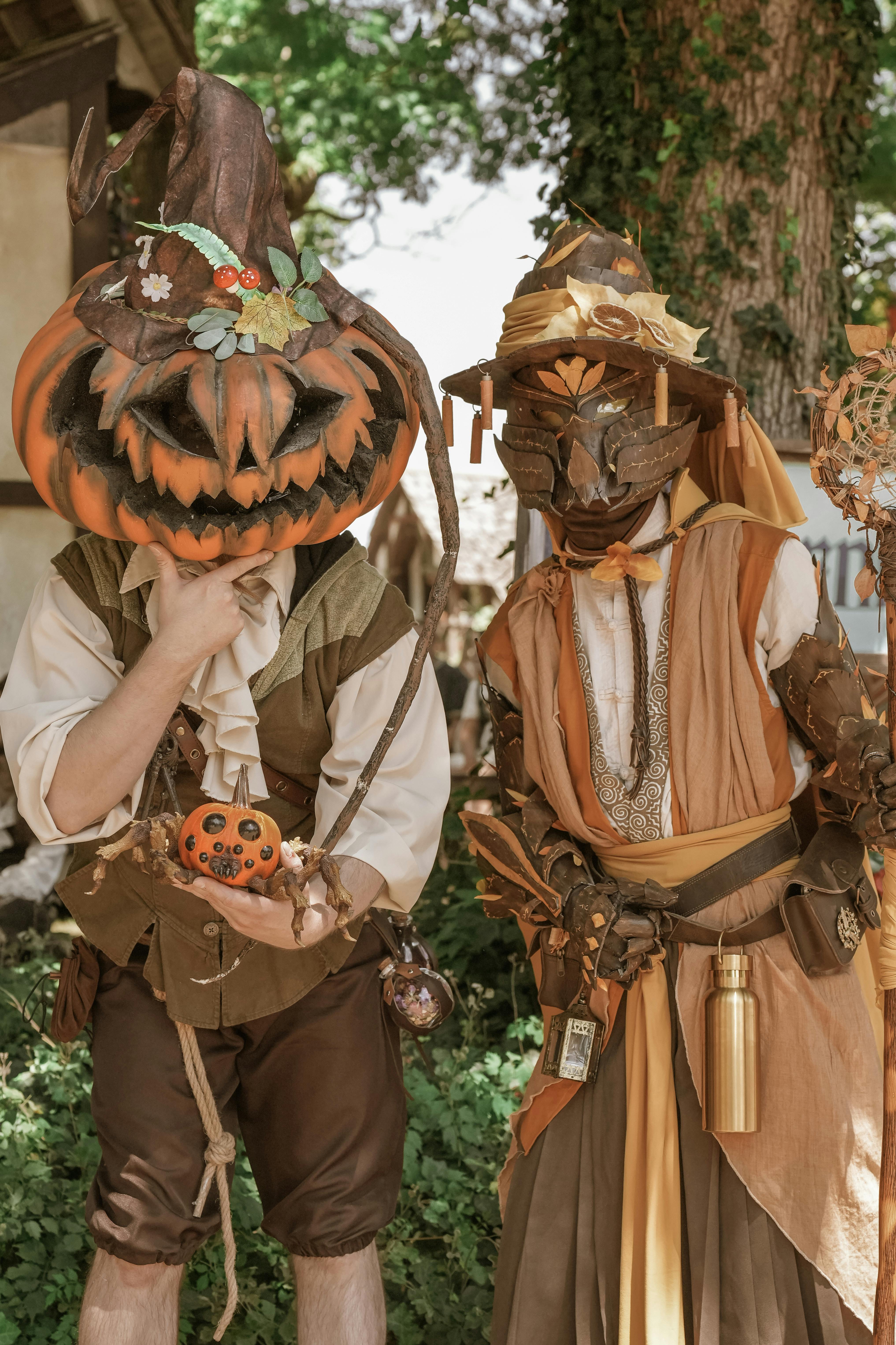 Two people in Halloween costumes as pumpkin and scarecrow characters outdoors.