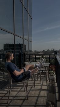 Man sitting on a balcony with cityscape view, enjoying a peaceful day.