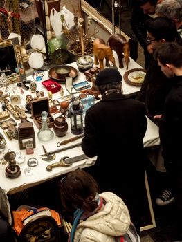 Shoppers exploring an antique market stall filled with various collectibles and vintage items.