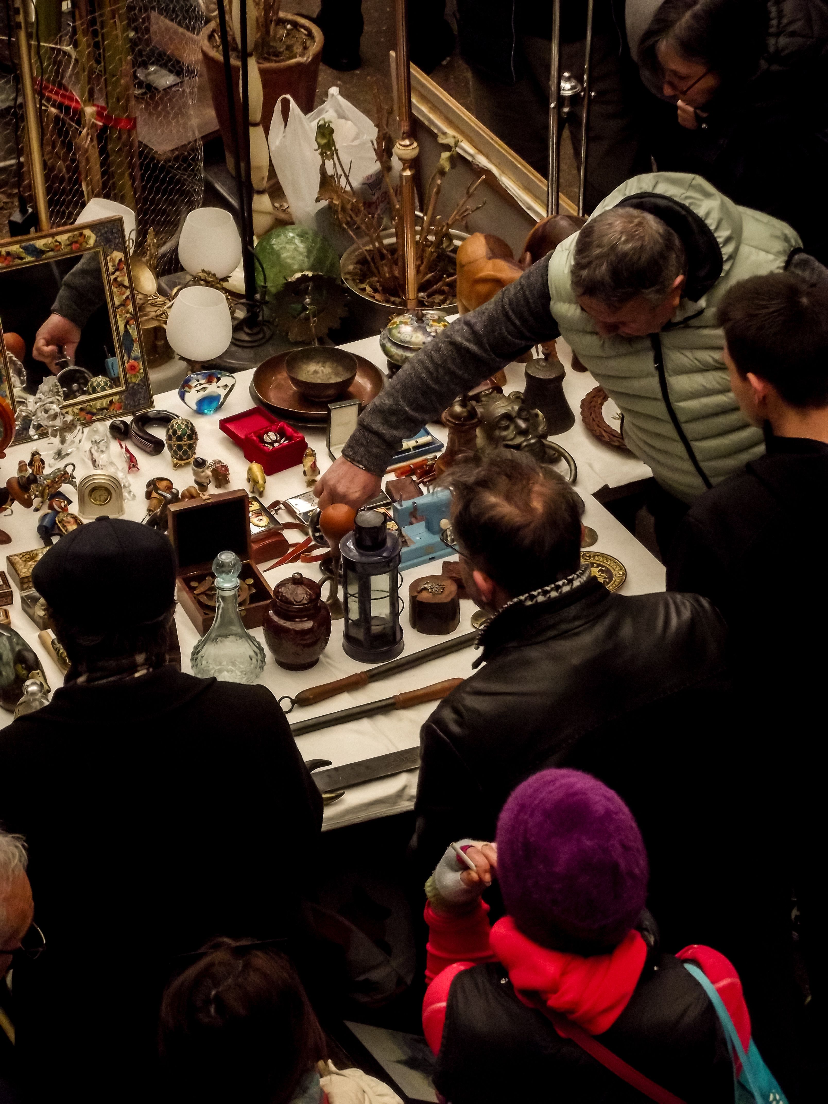 A bustling vintage market with people examining various antiques on display.