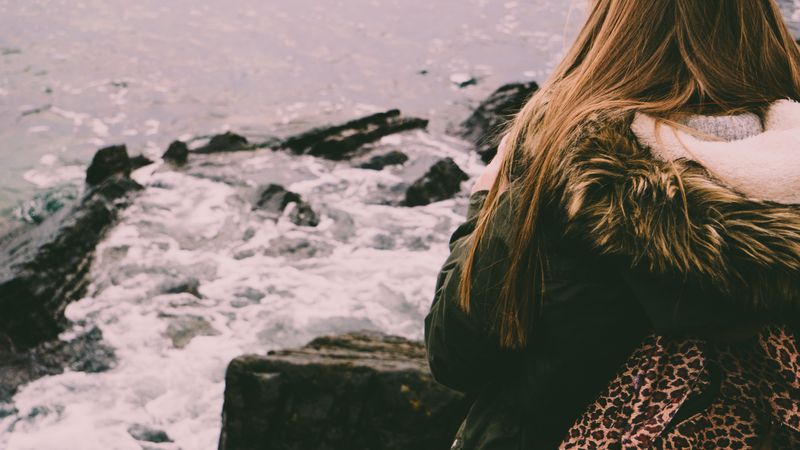 Woman in warm fur-lined coat by the shoreline
