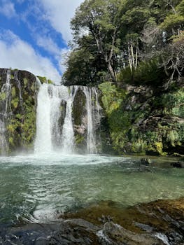 Beautiful waterfall surrounded by lush greenery under a vibrant sky in Villa La Angostura, Argentina.