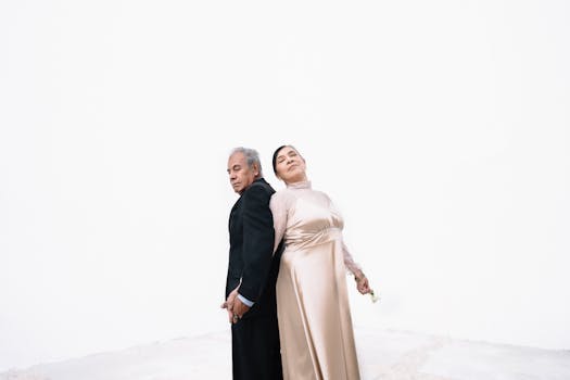 A senior couple elegantly posing in formal attire against a white background.