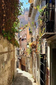 Sunlit narrow alley in Granada, Spain, with a view of the Alhambra palace.