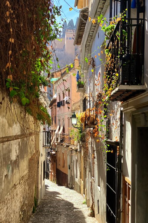 Free Sunlit narrow alley in Granada, Spain, with a view of the Alhambra palace. Stock Photo
