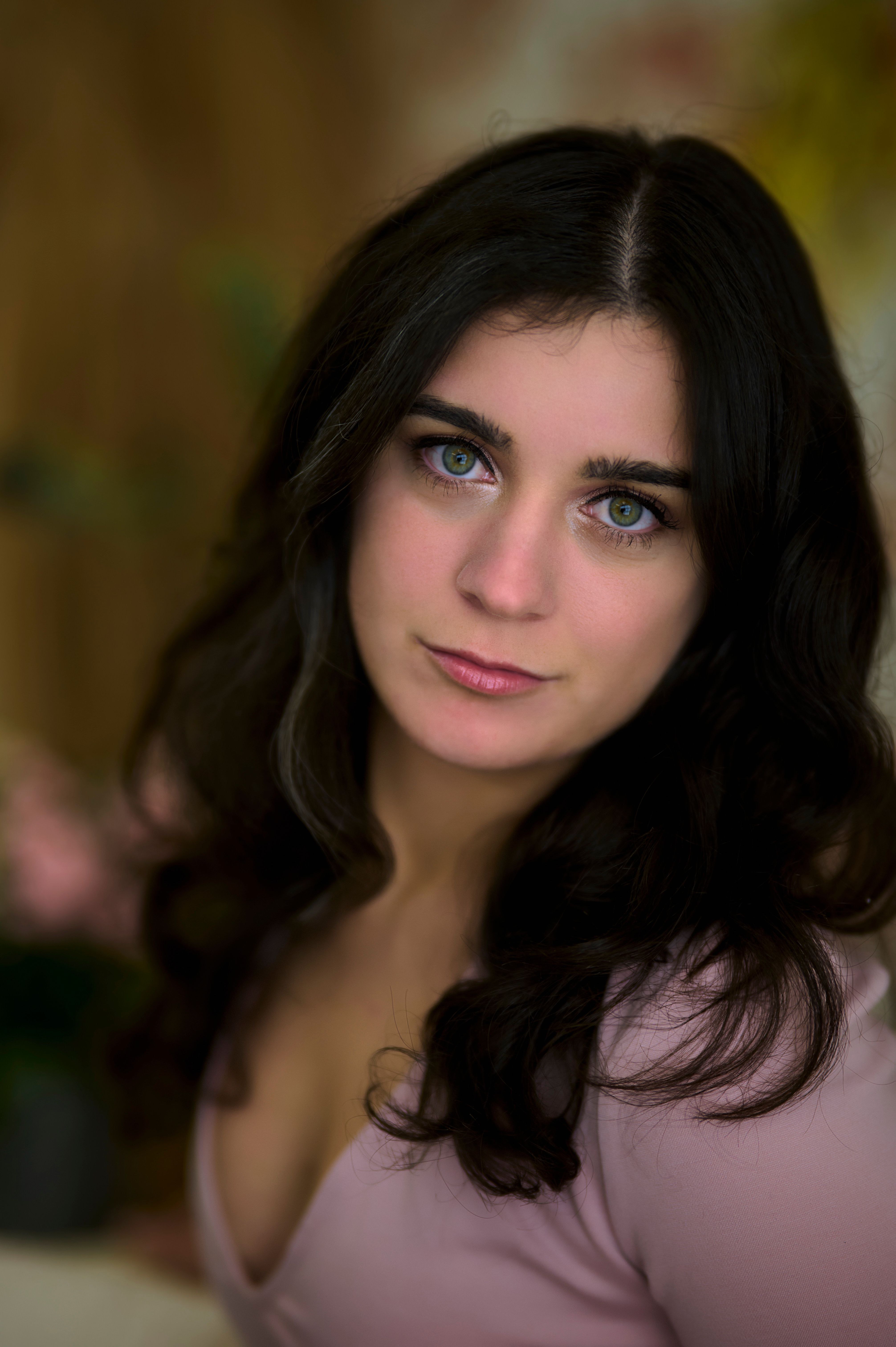 Portrait of a young woman with long dark hair and green eyes, soft indoor lighting.