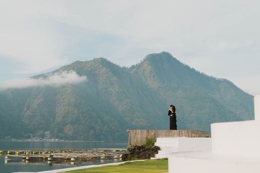 A couple embraces by the lake with stunning mountain scenery in Indonesia.