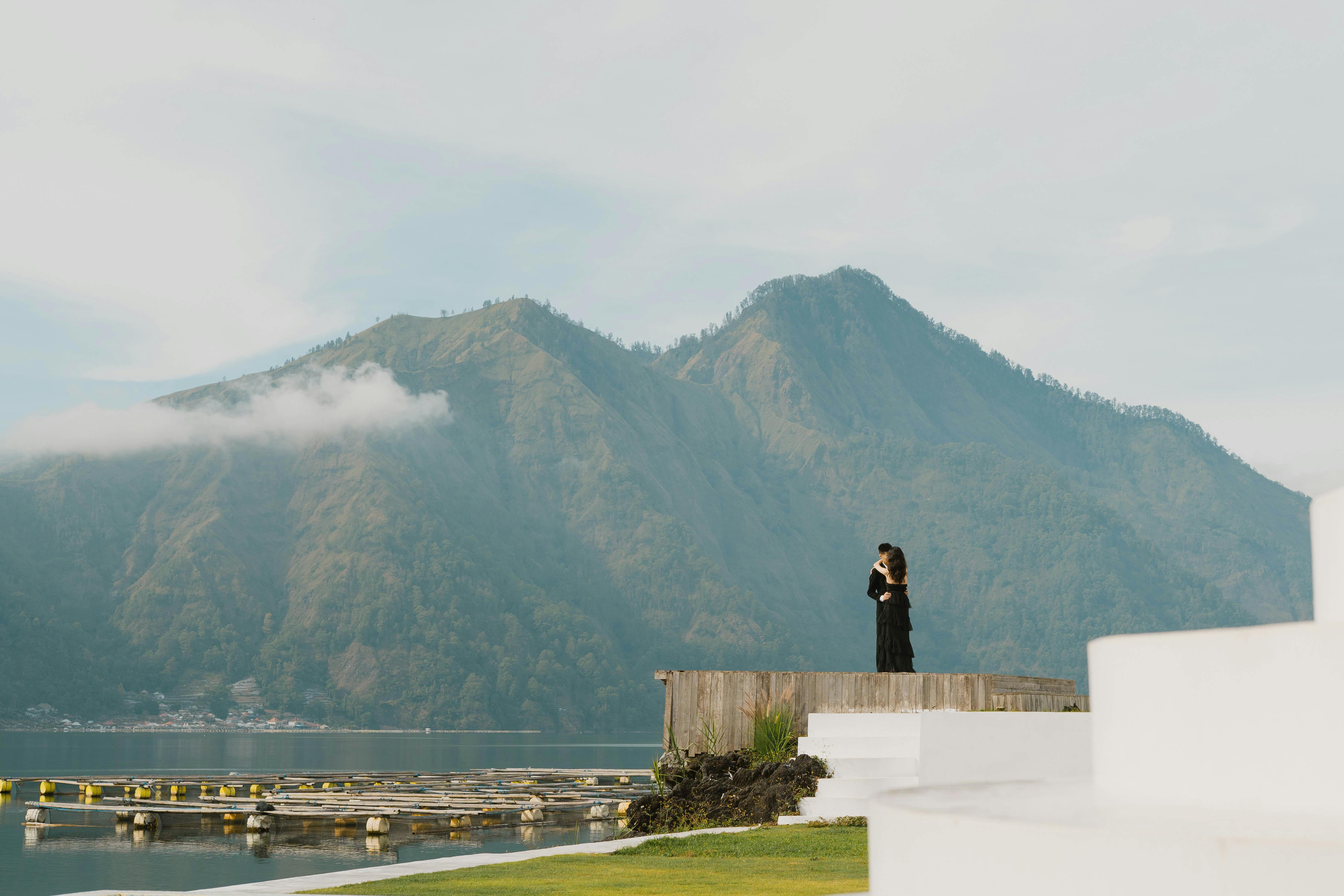 Free A couple embraces by the lake with stunning mountain scenery in Indonesia. 💖 Honeymoon Hotels & Resorts in Bali