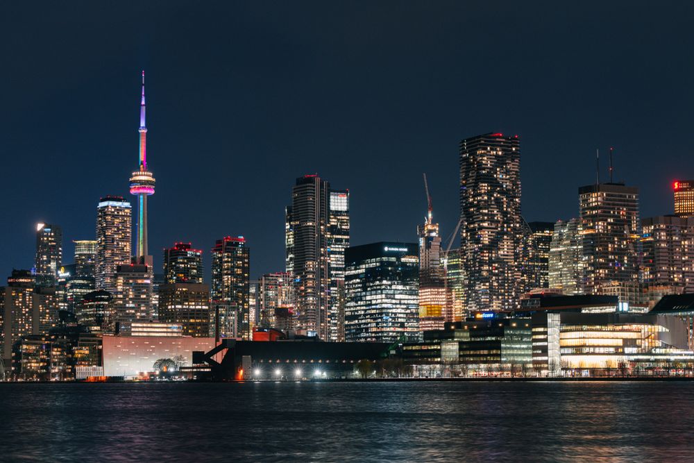 Vibrant night view of Toronto skyline featuring the illuminated CN Tower reflecting on the water.