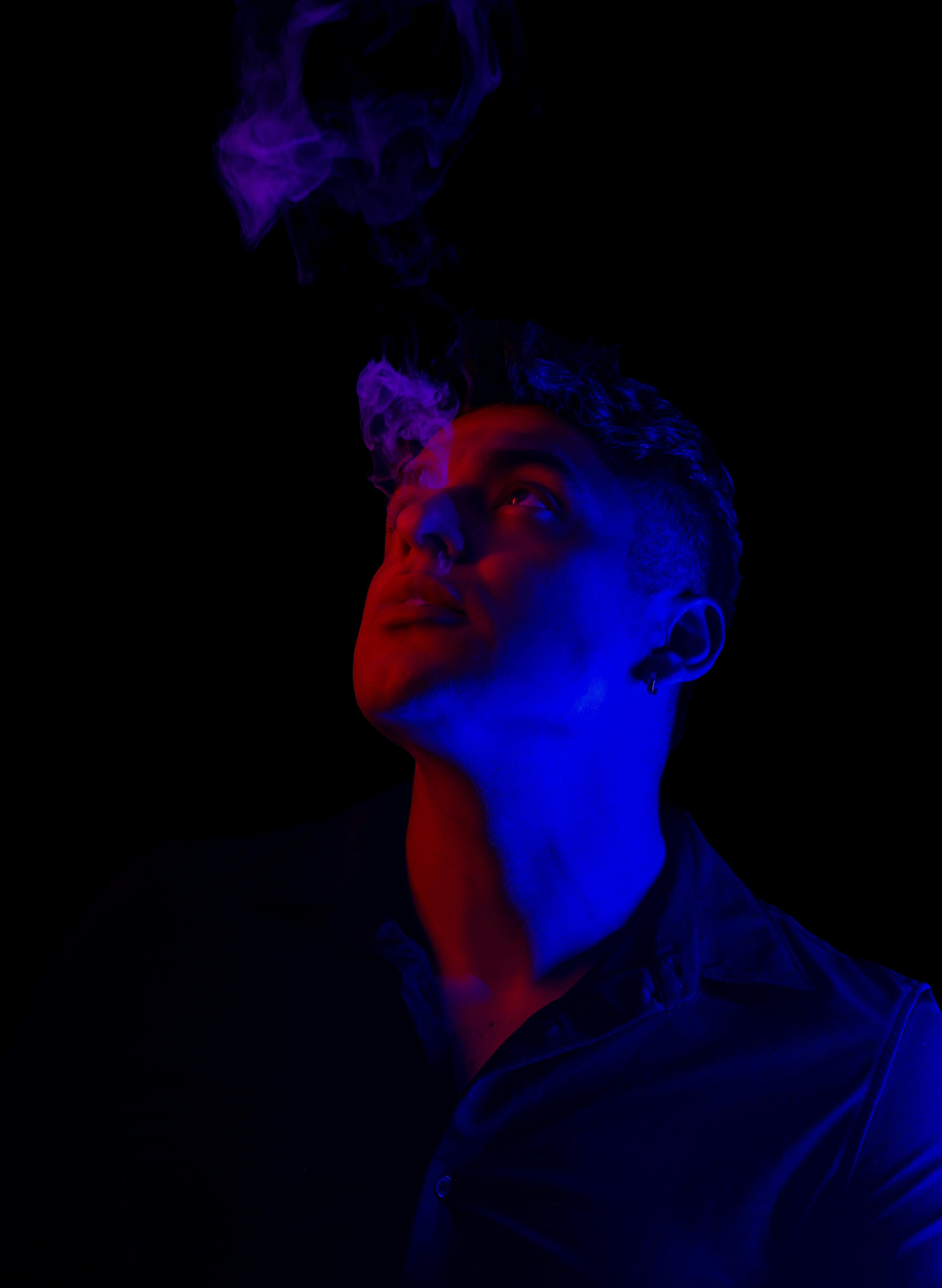 Dramatic portrait of a man looking up with colored smoke against a dark background.