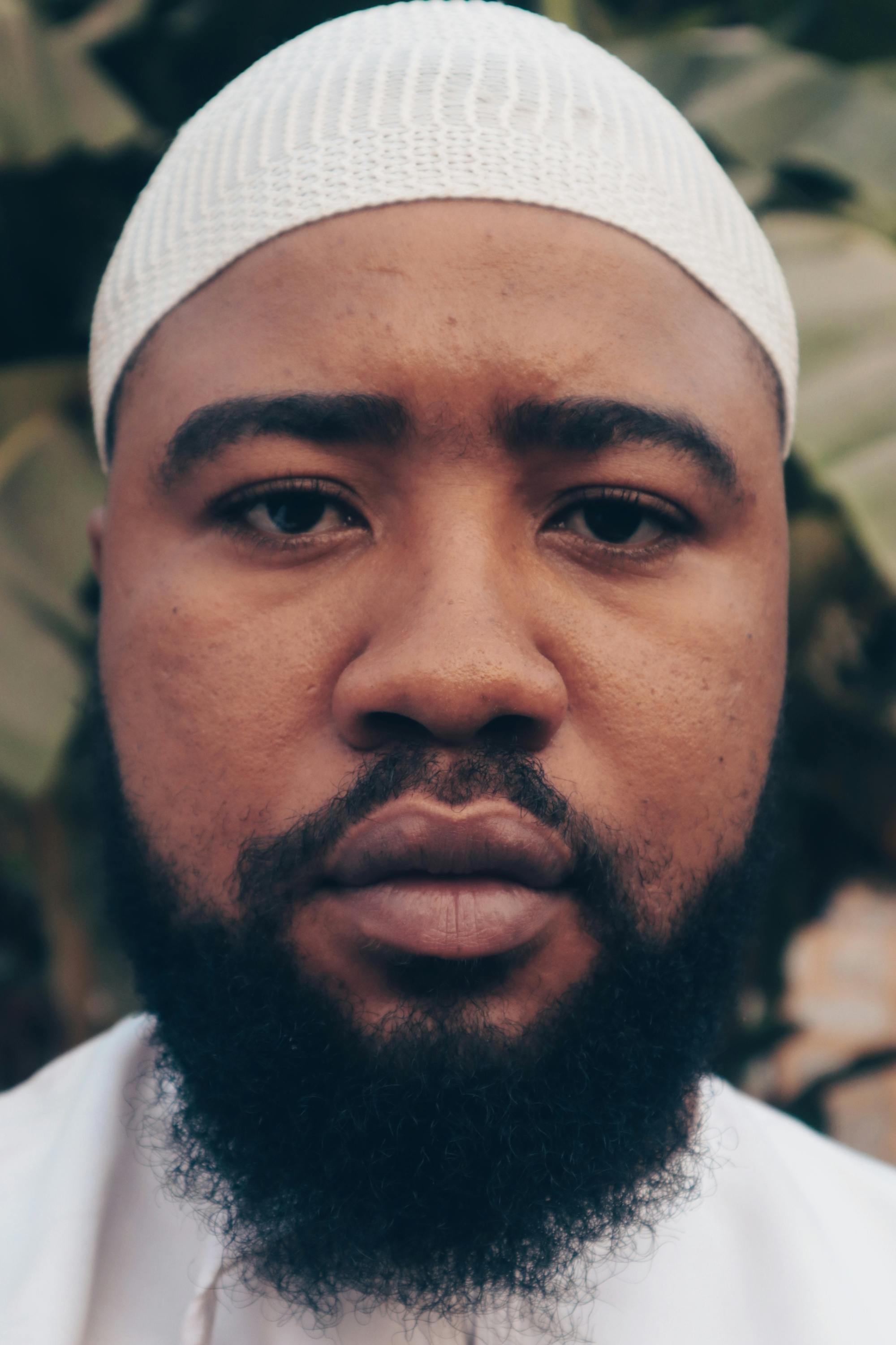 Close-up portrait of a man wearing a white cap, showcasing his facial features.
