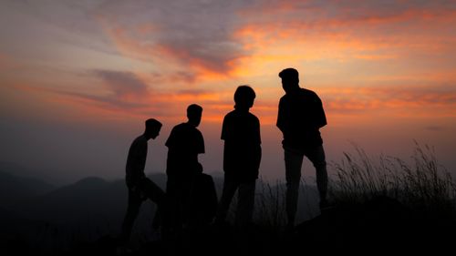 Free Silhouetted group of four people against a vibrant sunset sky. Stock Photo