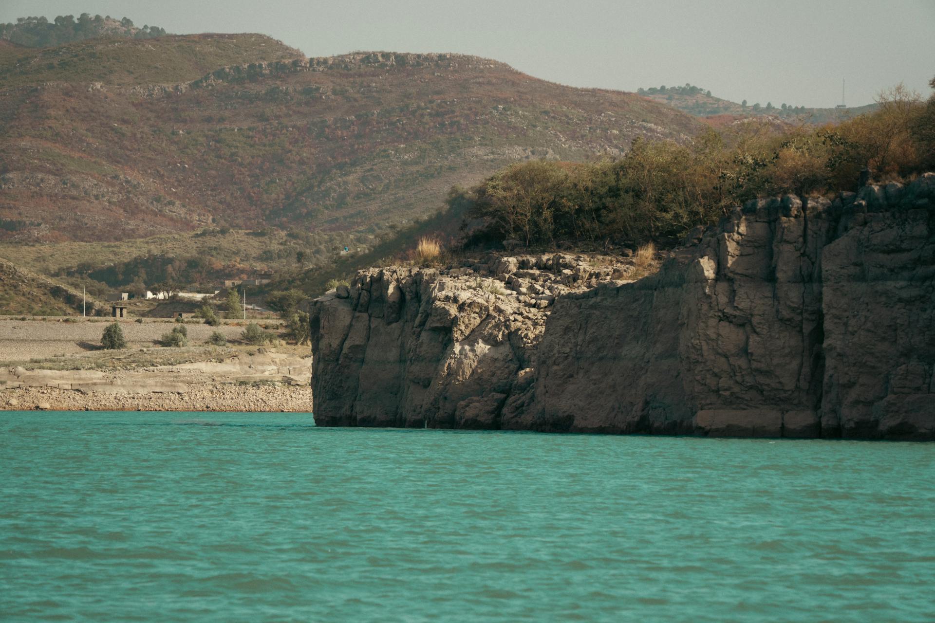 Peaceful turquoise lake with rocky cliffs and hills under clear summer sky.