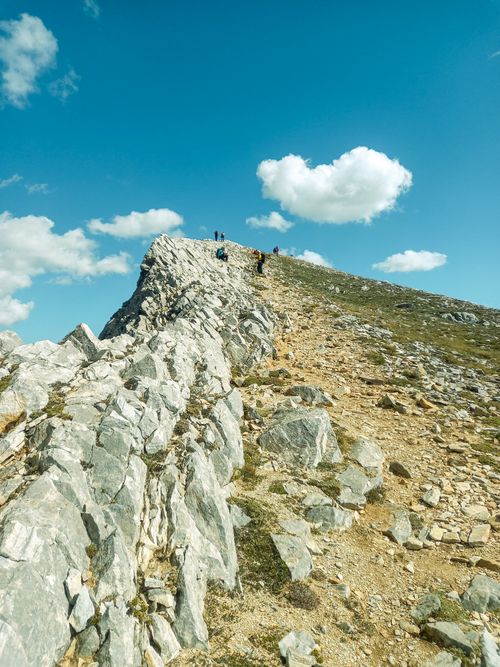 Free Scenic mountain ridge with hikers under a bright blue sky with fluffy clouds. Stock Photo
