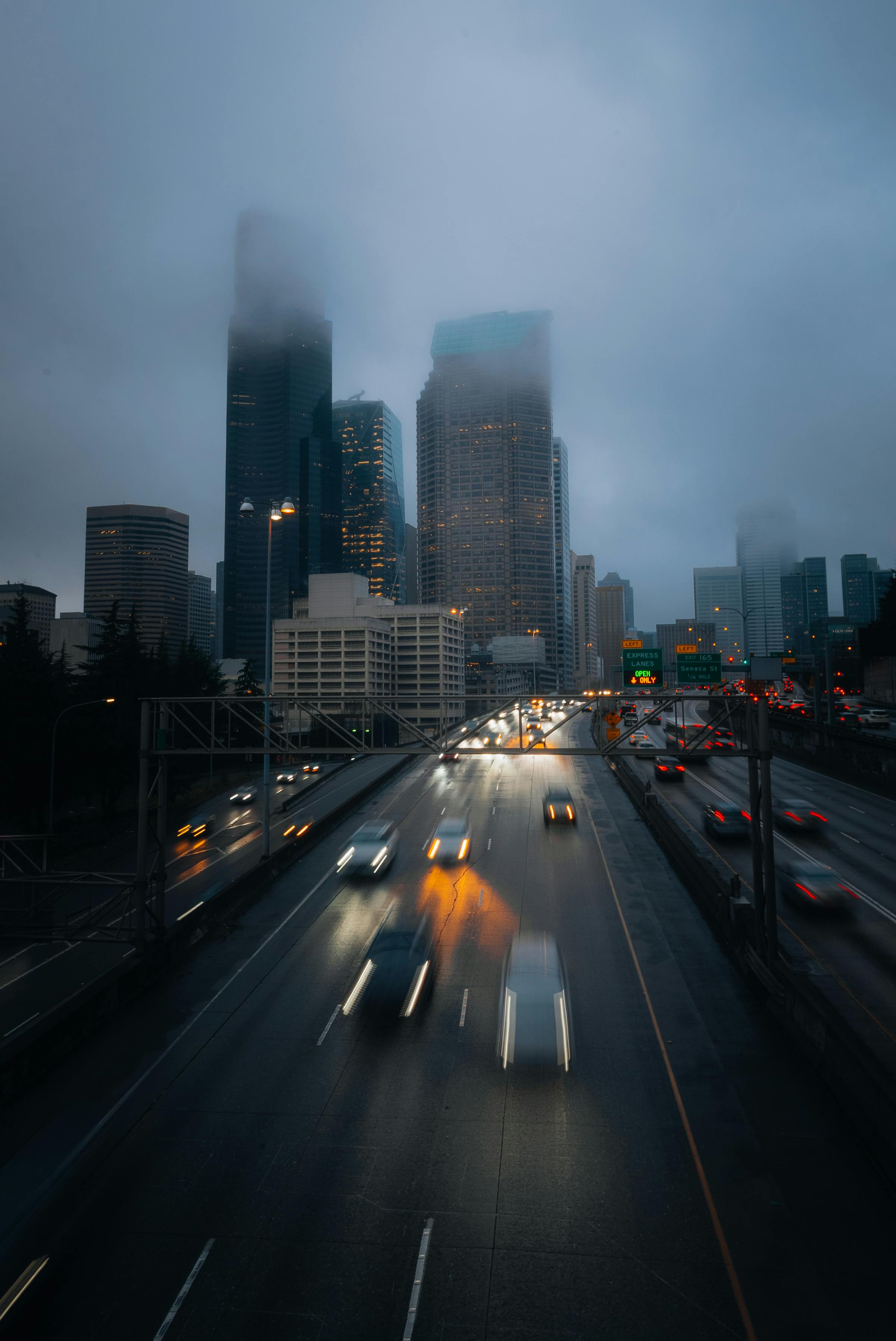 A foggy evening view of Seattle's skyscrapers with blurred car lights on the highway.