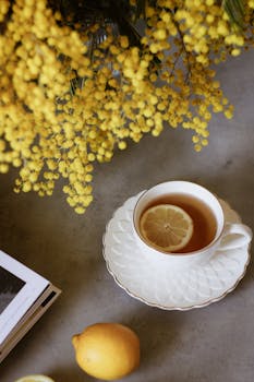 Cozy tea scene featuring a cup with lemon slice and yellow mimosa flowers.