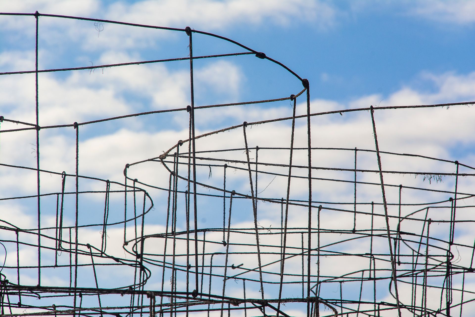 Abstract view of metal structures silhouetted against a cloud-filled blue sky.