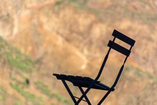 A silhouette of a bistro chair with a blurred earthy and green natural background.