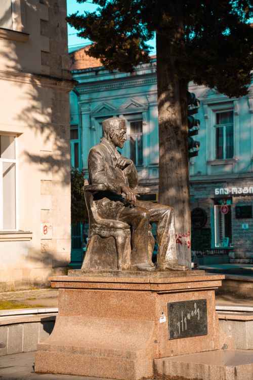Free A bronze statue of a man seated in a city square, capturing urban architectural elements. Stock Photo