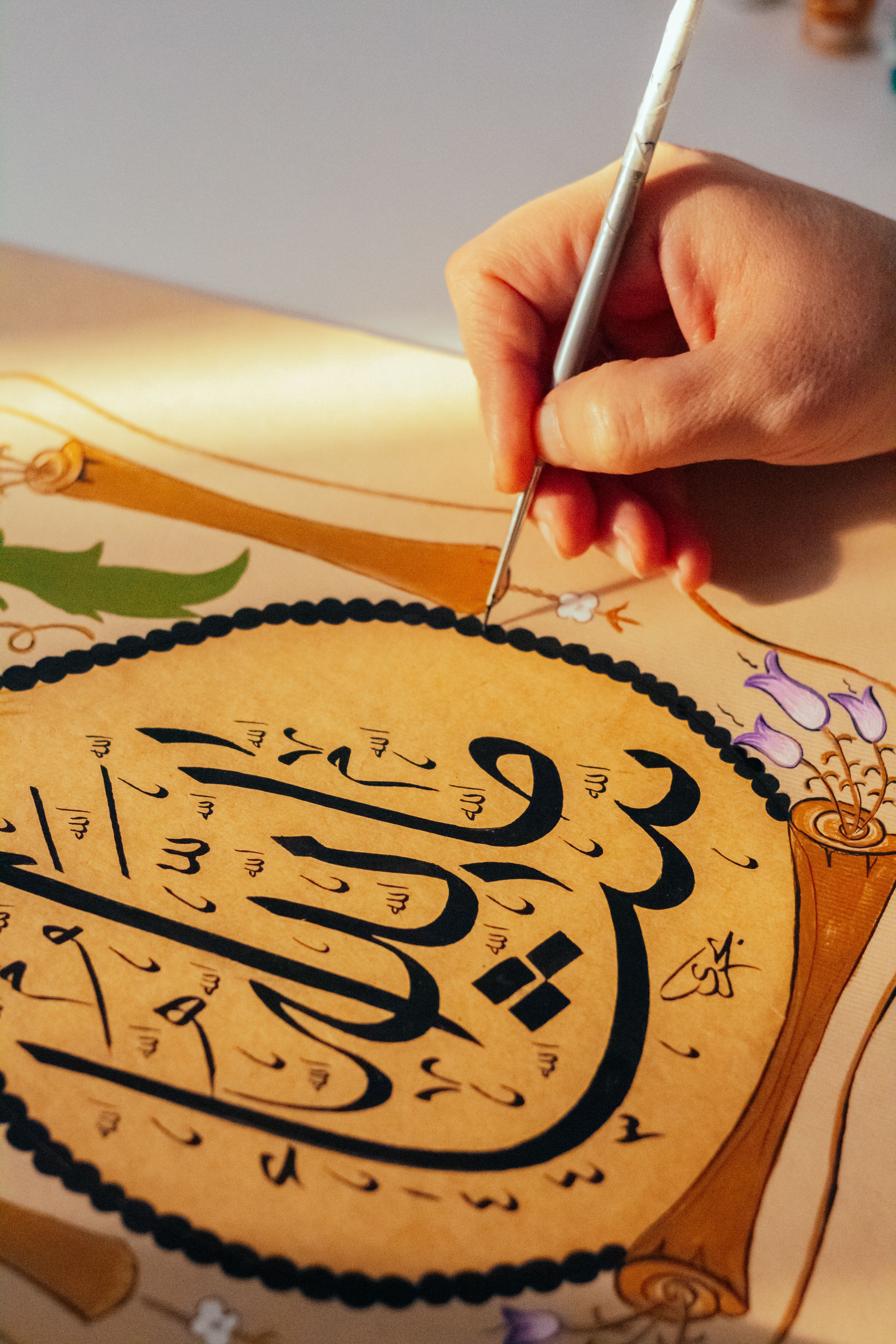 Close-up of hand painting Arabic calligraphy with intricate details.