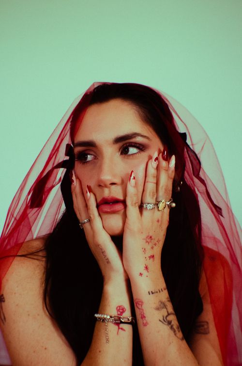 Free A woman in a red veil with expressive makeup and tattoos, reflecting deep thought. Stock Photo
