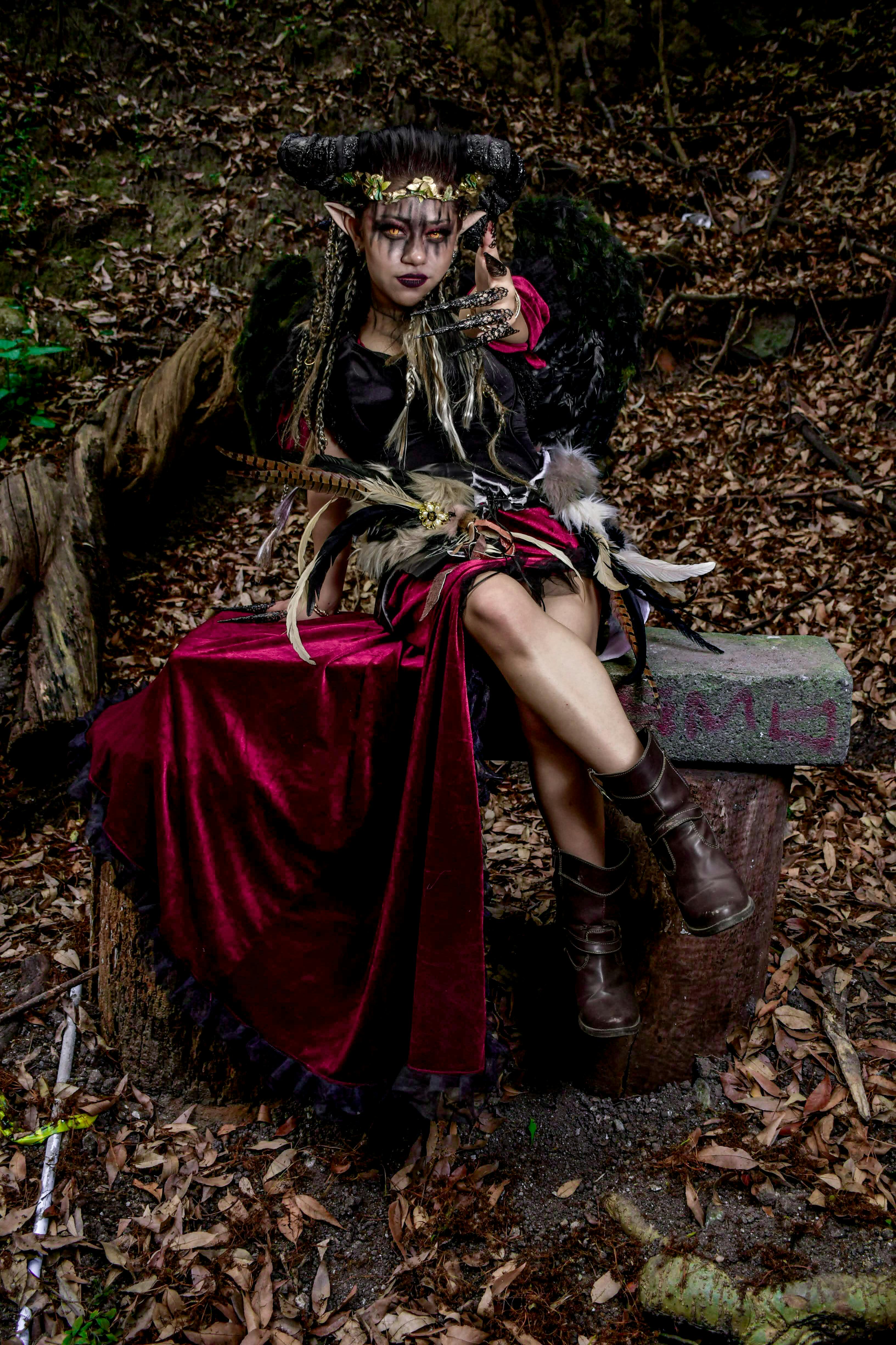 grátis Uma mulher em traje de fantasia detalhado está sentada no toco de uma árvore em uma floresta, evocando temas míticos. Foto profissional