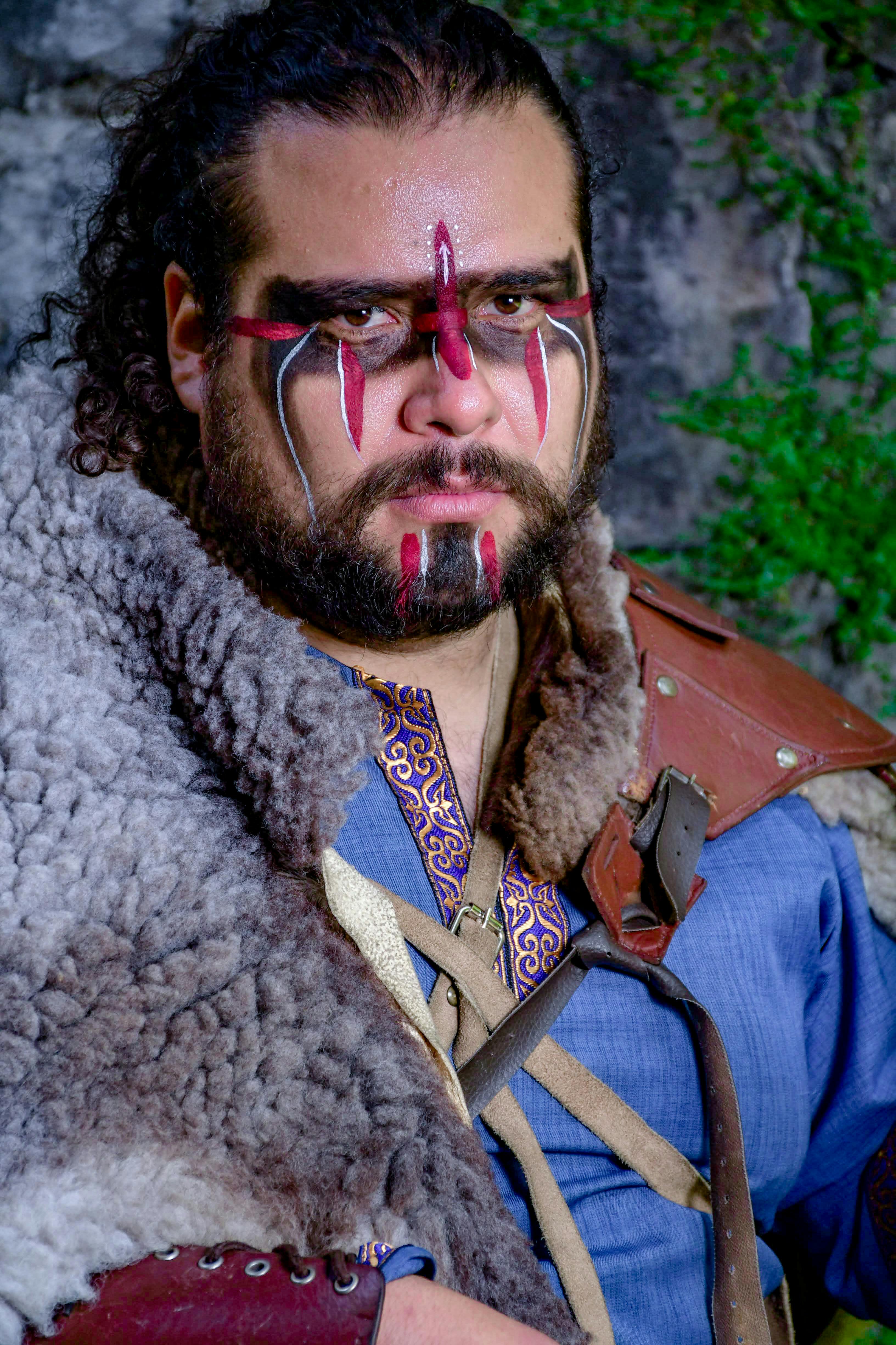Portrait of a man in rustic attire with tribal face paint, evoking a historical or fantasy theme.