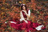 一位身着红色连衣裙的年轻女子，优雅地坐在秋叶绚烂的景致中