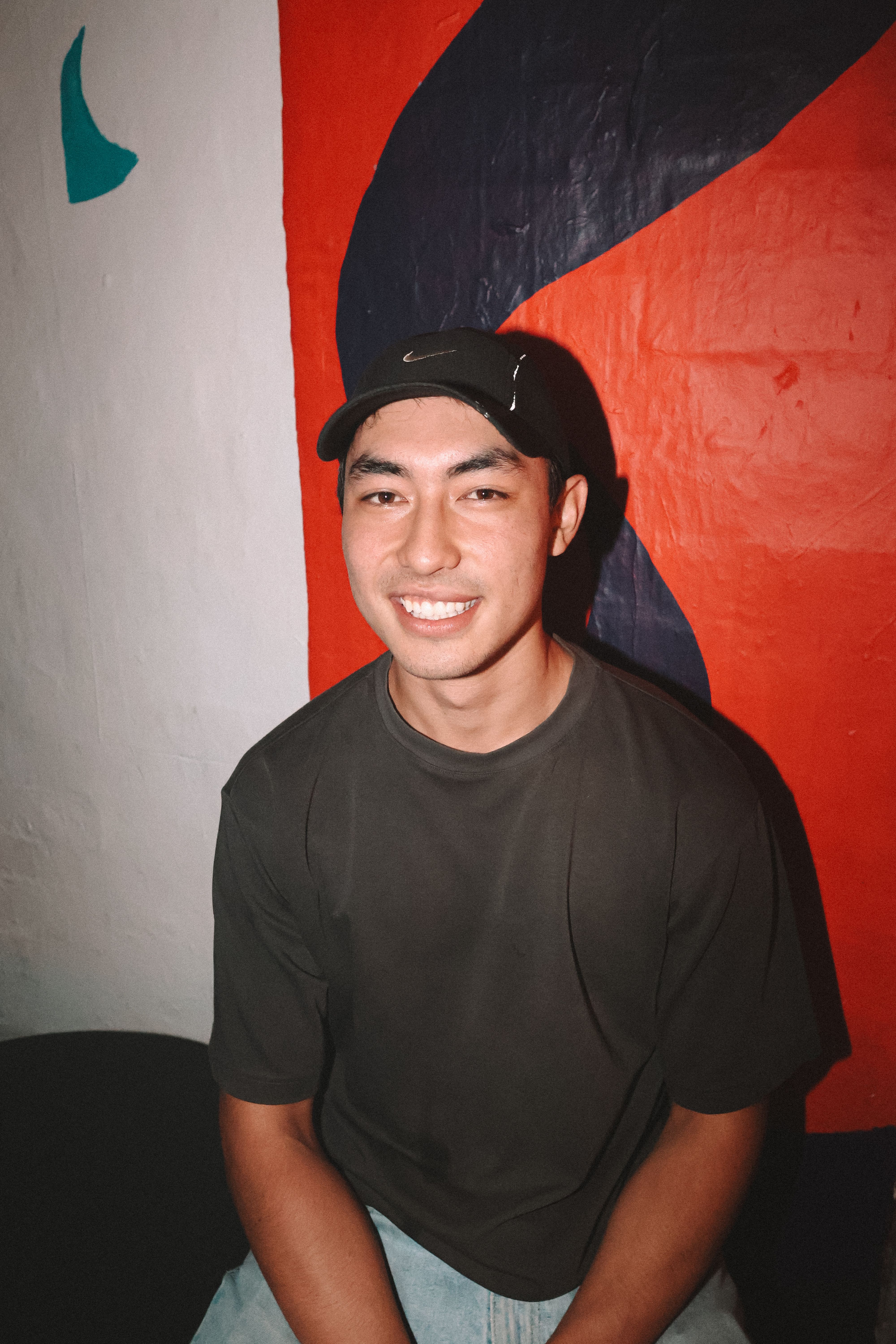 A relaxed, smiling man sitting indoors against a vibrant abstract mural. Ideal for lifestyle and people content.