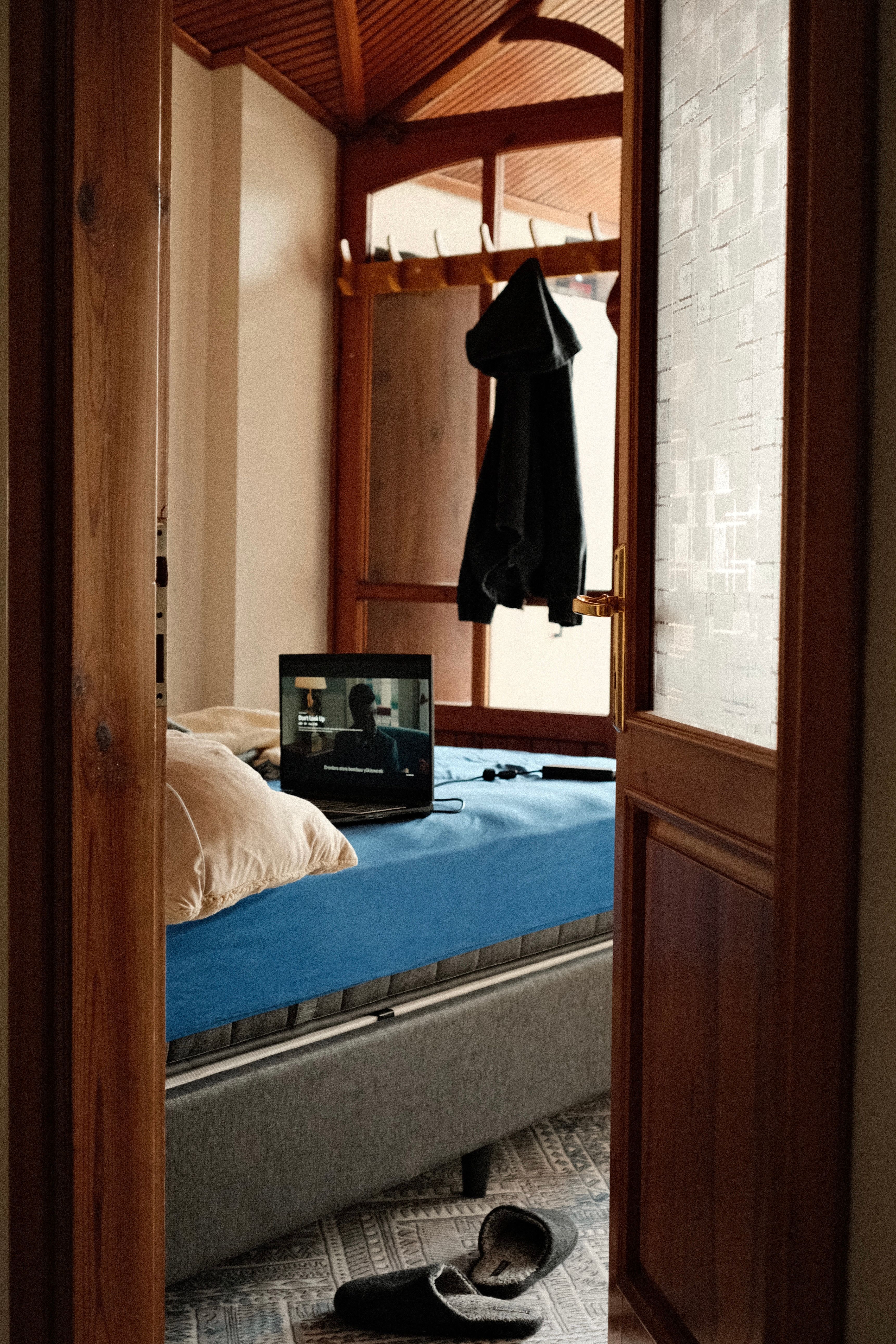 Warm bedroom interior with TV on blue bed, open door view.