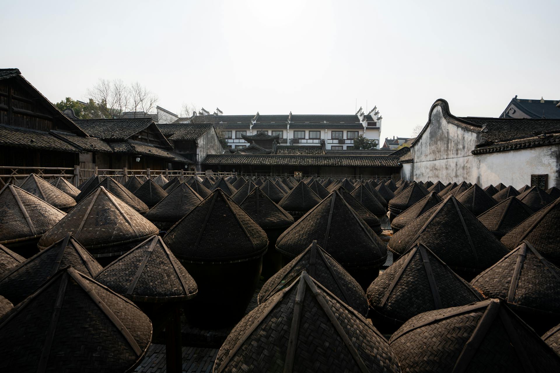 Rows of traditional Chinese pottery jars under wooden roofs in a historical courtyard setting.