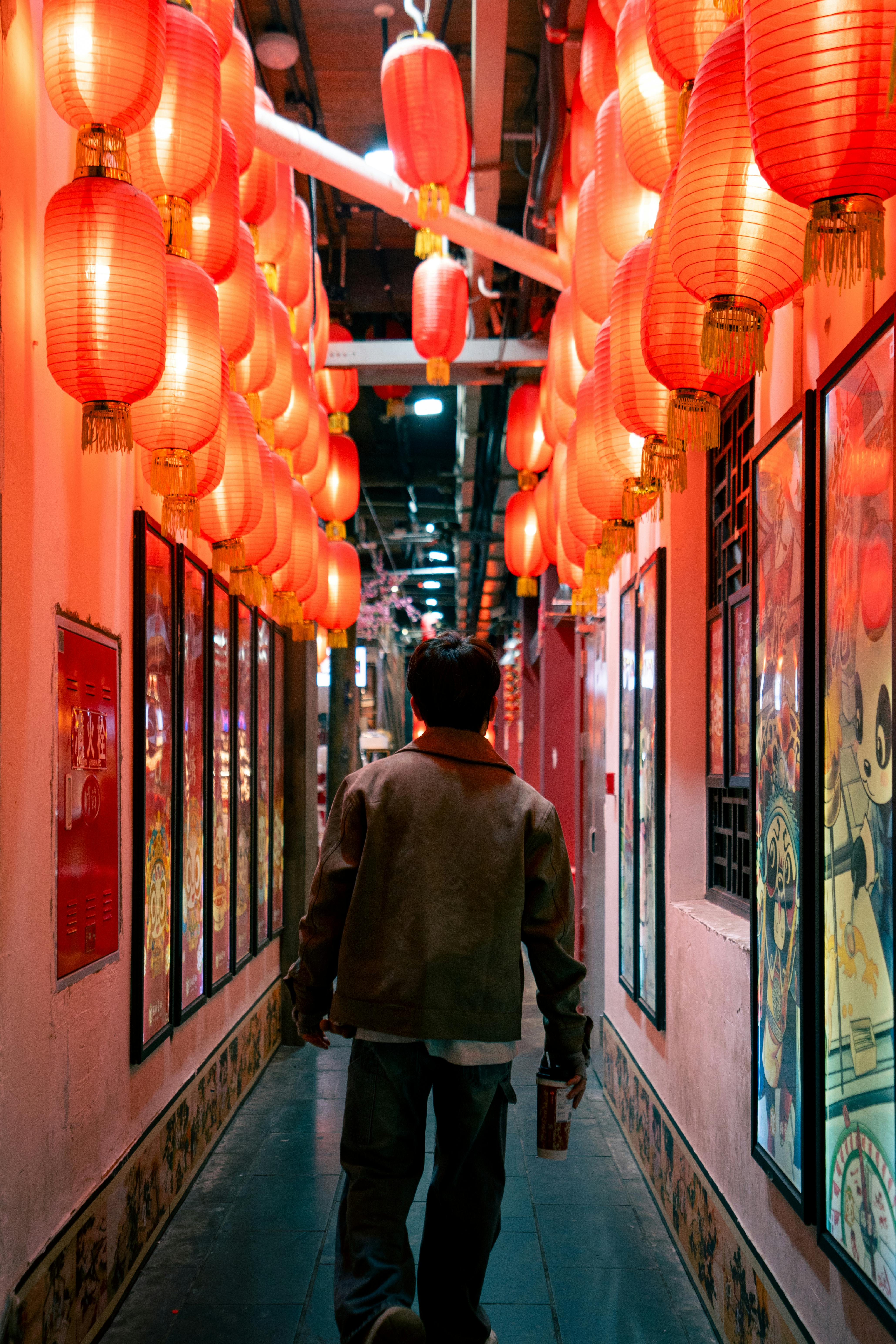A man walks through an alley adorned with vibrant red lanterns at night.