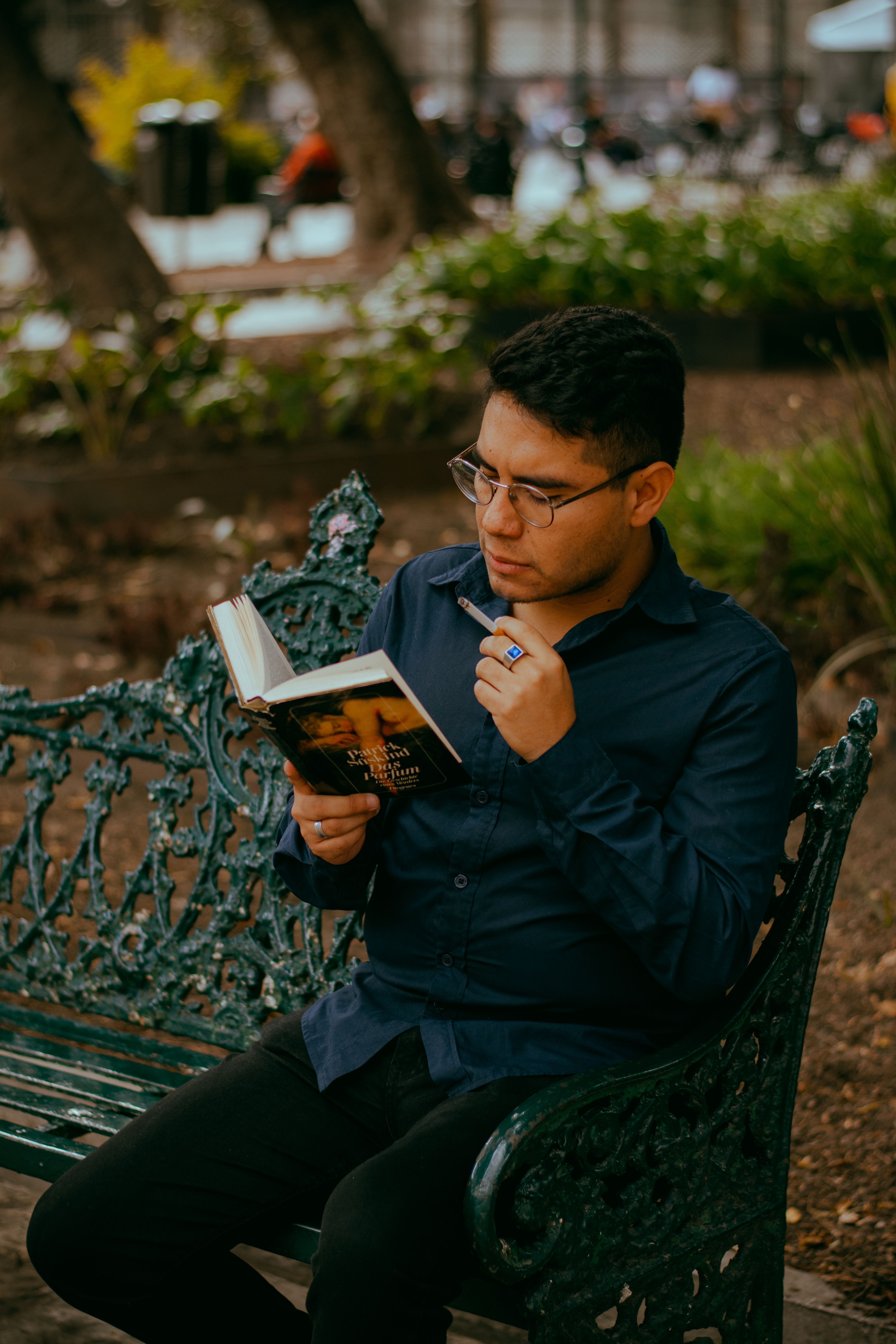 A contemplative young man reading a book while seated on a decorative park bench outdoors.