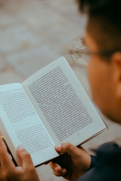 Free A person reading a book outdoors in natural sunlight, focusing on relaxation and literature. Stock Photo