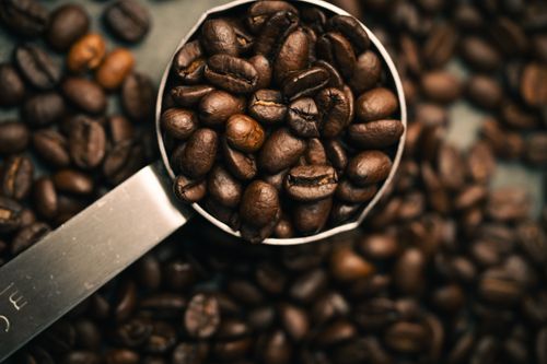 Free Detailed close-up of coffee beans filling a metal measuring scoop, with scattered beans in the background. Stock Photo