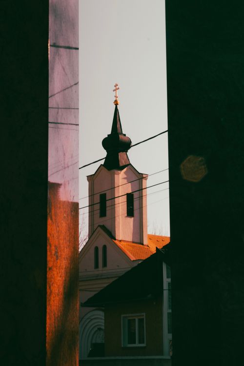Free Dramatic view of a church tower framed by dark structures at sunset. Stock Photo