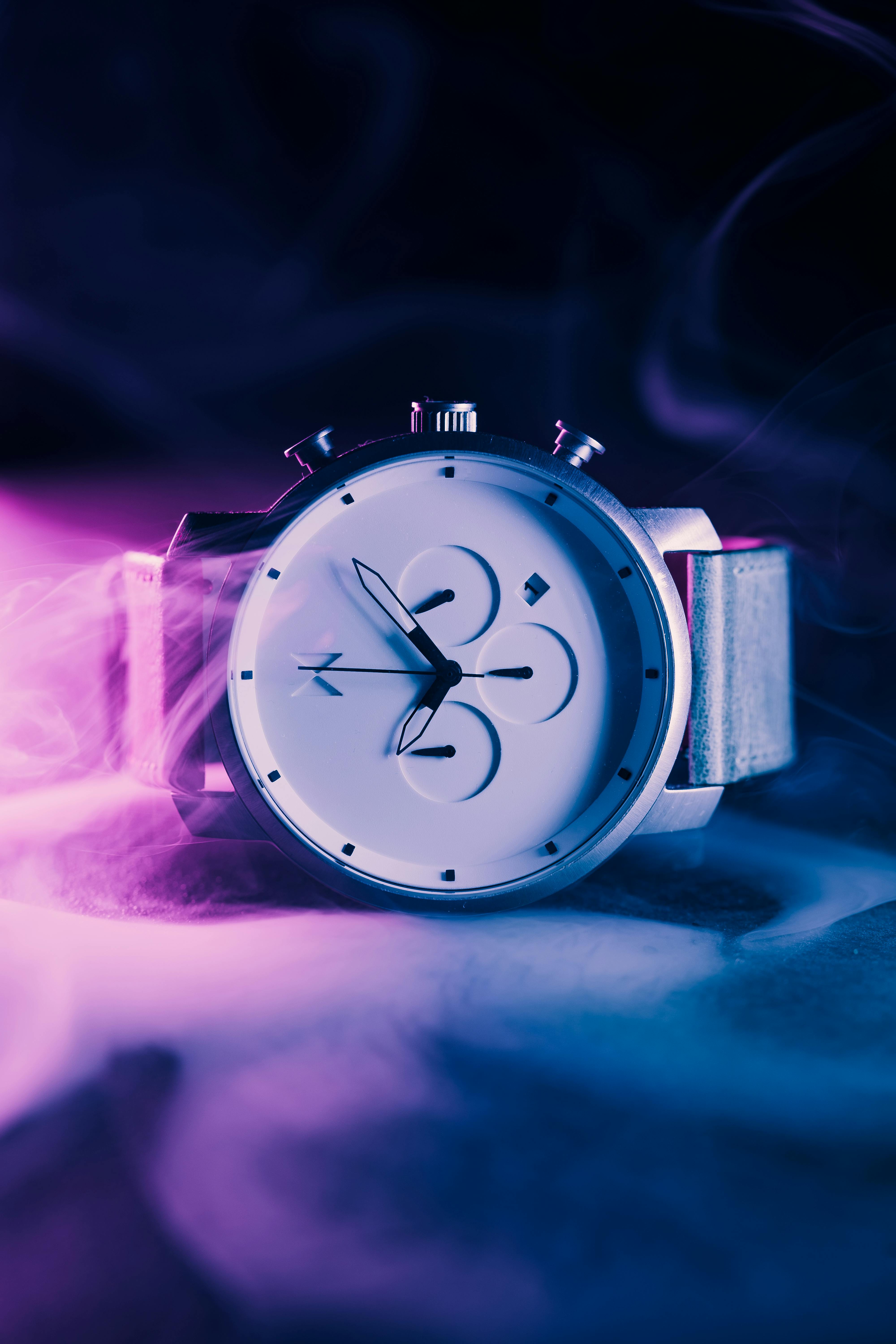 Free Close-up of a modern wristwatch with a sleek design enveloped in a vibrant purple glow. Stock Photo