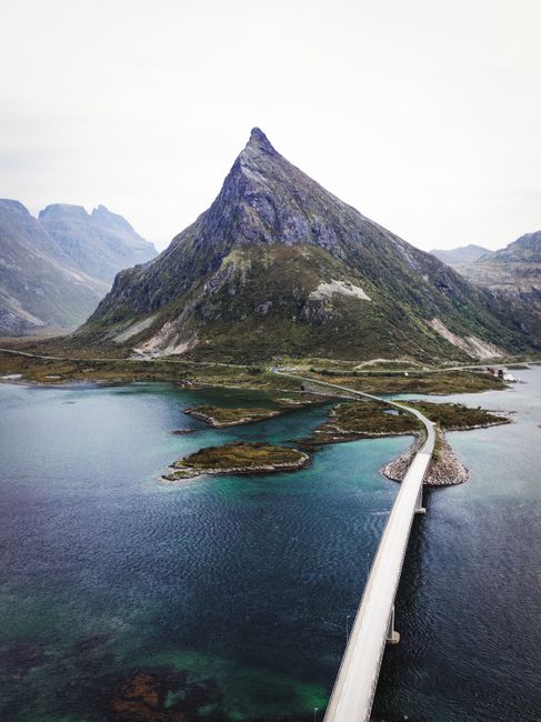 A serene view of a bridge connecting islands in the Lofoten region, with a majestic mountain in the background.
