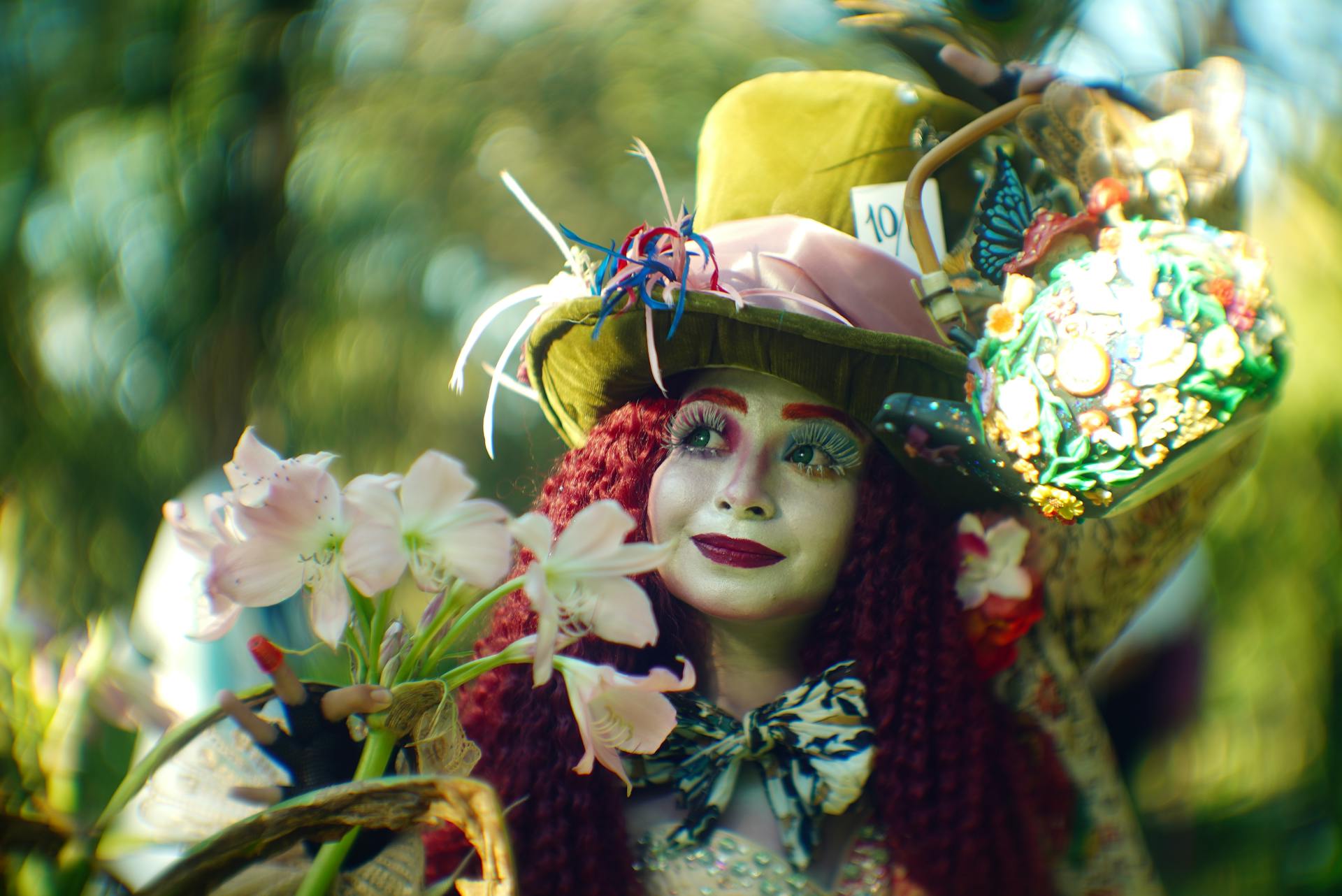 Whimsical Mad Hatter character posing with flowers and props in colorful outdoor setting.