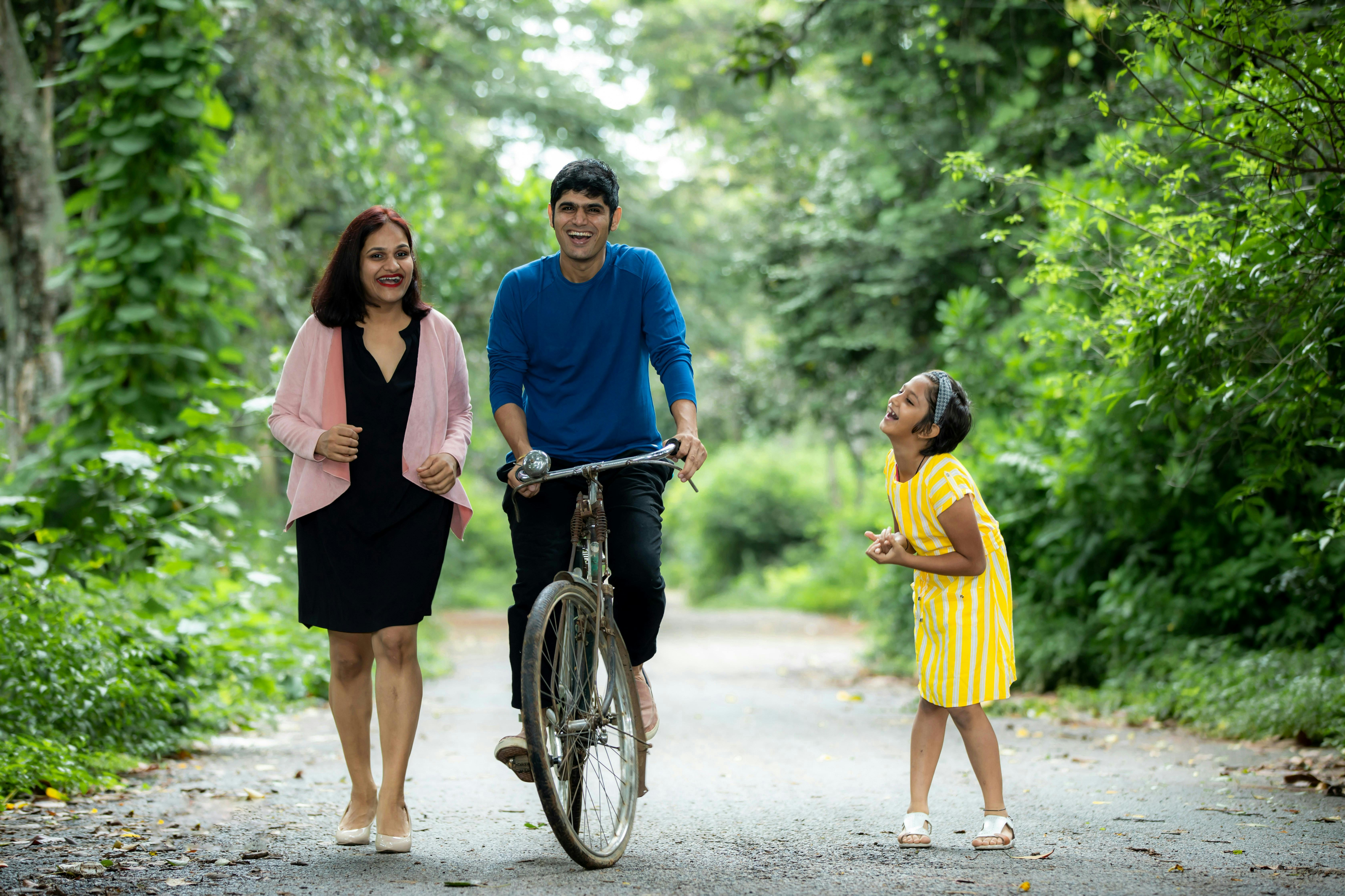 A joyful family enjoying a walk with a bicycle on a green forest path.