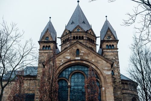 Free Exterior view of a Gothic-style church in Düsseldorf with three towers and intricate windows, framed by barren trees. Stock Photo