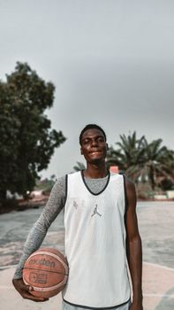 A young basketball player holding a ball on an outdoor court in Nigeria.