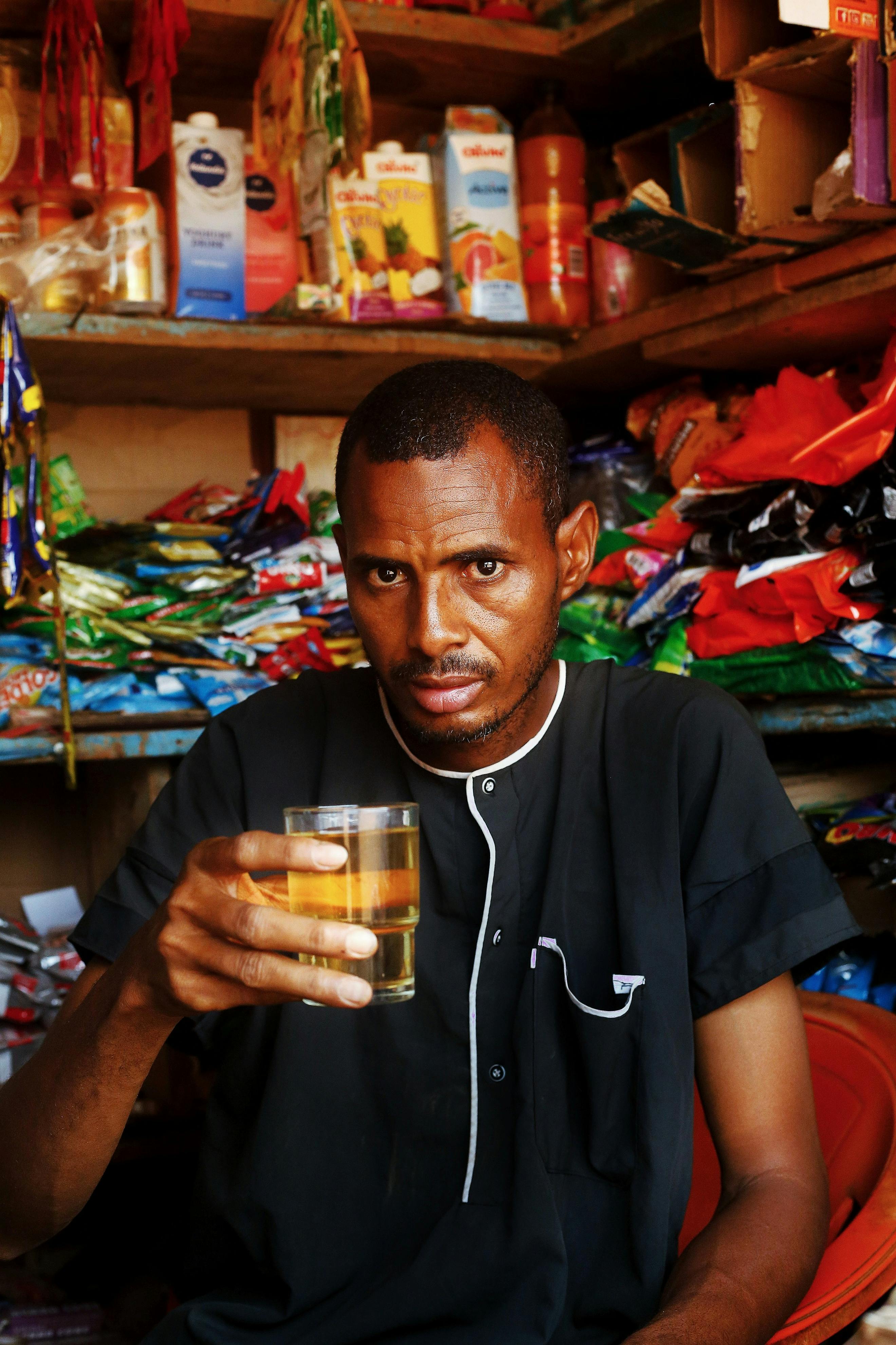 An adult man holding a glass of drink in a vibrant market in Abuja, Nigeria.